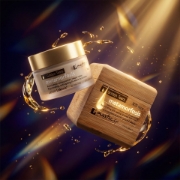 Artistic display of Metamorfosis cream jar and box with golden oil droplets representing the 50% antioxidant boost of Lakesis.