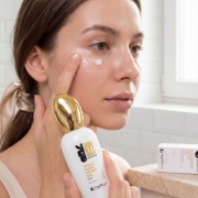 Close-up of a young woman with glowing skin, applying Mastic Spa Hyaluronic Velvet Eye Gel under her eye with her fingertip for lifting, firming, and brightening effects.
